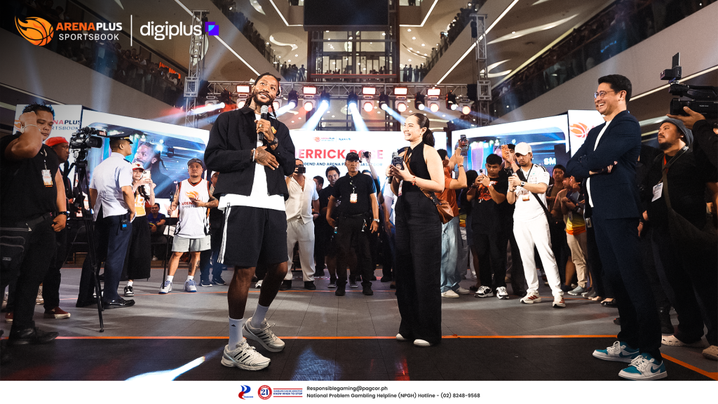 Derrick Rose speaking on stage at a crowded ArenaPlus event with event staff, presenters, and fans gathered around him.